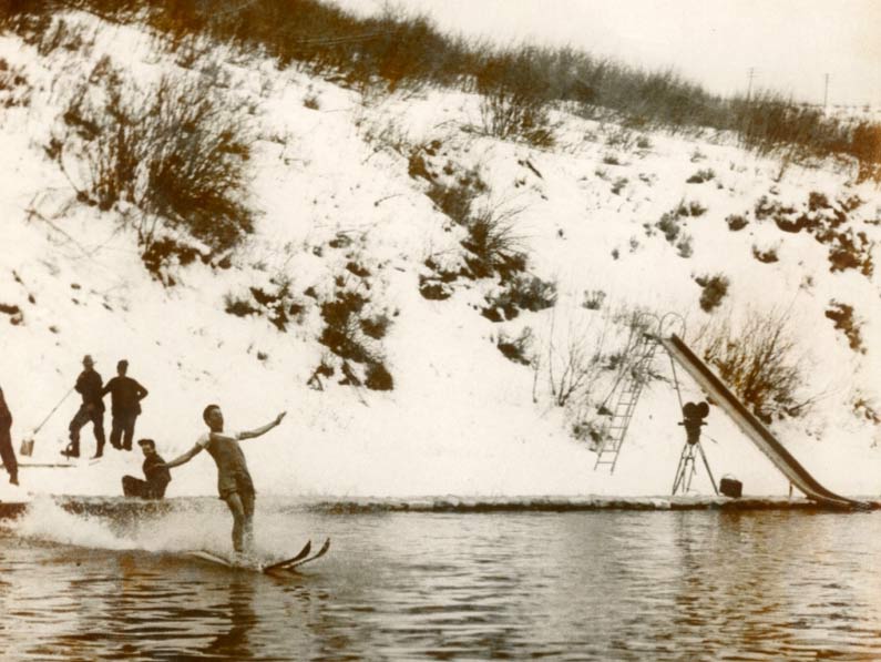 Man skiing off of snowy hillside into a warm pool of water at the Old Town Hot Springs in 1940.