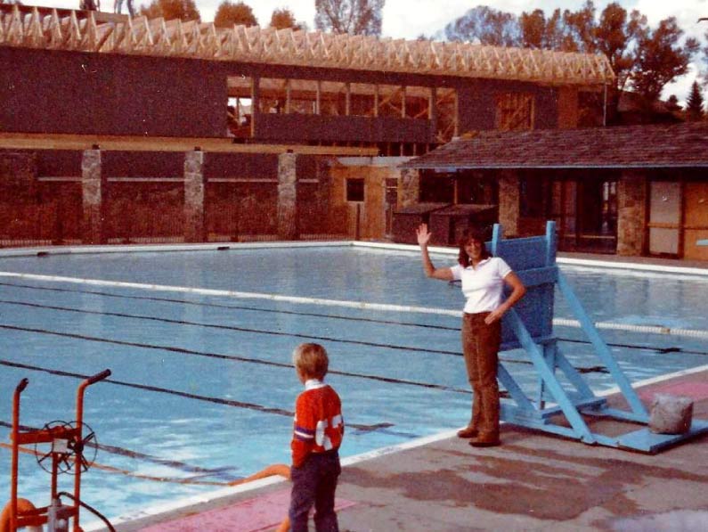 Women waves to the camera in 1983 with building being built in front of the pool.