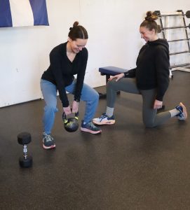 female personal trainer helping client with a kettle bell squat