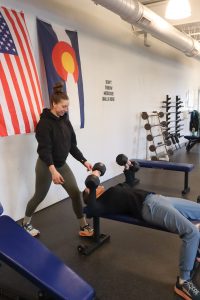 female personal trainer helping client with overhead press on an incline bench