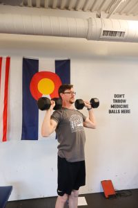 personal trainer demonstrating a shoulder press with two dumbbell weights