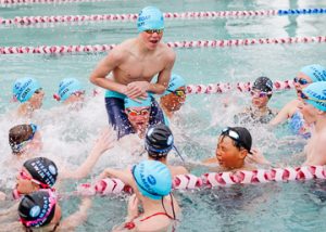 kids splashing and cheering in the lap pool with swim caps on