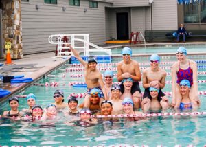 Group swim team photo with boys and girls smiling in the lap pool
