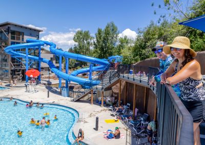 A mom and her dad smile and look over the deck to the pools below on a summer day at the hot springs.